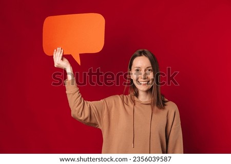 Studio portrait of a young smiling woman holding an orange bubble speech over red background.
