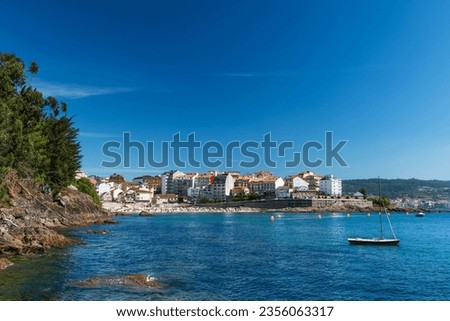 Wide-angle view of a beautiful crowded beach in Portonovo in the Ria de Pontevedra, Spain, on a sunny summer morning with a clear blue sky.