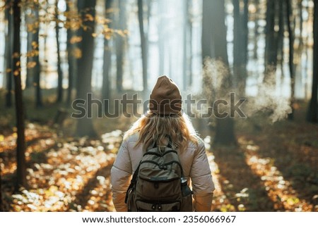 Foggy cold morning weather in autumn. Woman with backpack and knit hat hiking in forest at fall season Royalty-Free Stock Photo #2356066967
