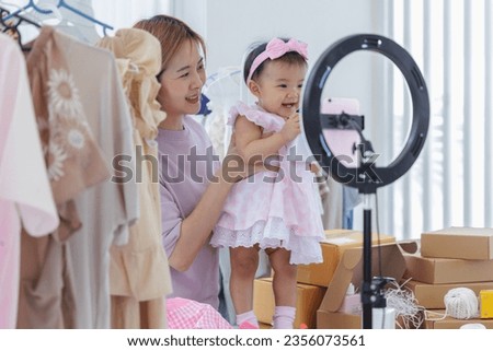 Asian young adult online seller, who adeptly combines work and motherly duties. Women is happy presenting products via live broadcasting use smartphone, all while tenderly taking care of adorable baby