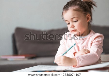 Cute smiling little girl write homework  at desk at home. Happy preschooler writing with left hand indoors. Children education concept. Royalty-Free Stock Photo #2356074107