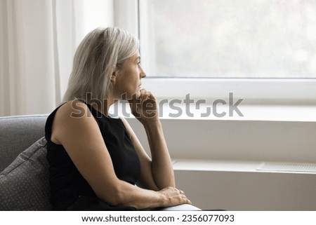 Thoughtful depressed mature woman sitting on couch at home, looking at window away in deep thoughts, suffering from depression, apathy, emotional crisis, thinking over problem, loss Royalty-Free Stock Photo #2356077093