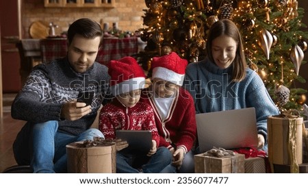 Addicted to modern technology happy family couple with kids using different gadgets, watching funny Christmas cartoons, spending time online, playing games, New Year winter holiday celebration.
