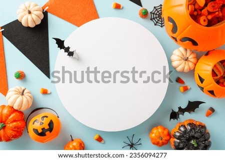 Enchanting children's trick or treat festivity. Bird's-eye top perspective capturing pumpkin basket with treats and Halloween decorations on blue isolated background, ample space for text or advert