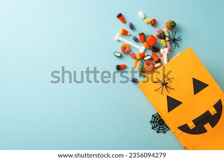Experience magic of kids' Halloween treat tradition. Top-view shot featuring pumpkin basket, sweets and Halloween decorations on an blue isolated surface, suitable for text or promotional material