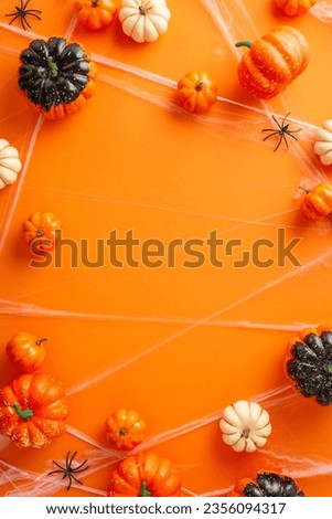 Mysterious Halloween event inspiration. Top view vertical picture highlighting pumpkins, spiders and spider web around on an orange isolated background, copy-space for text or advertising elements