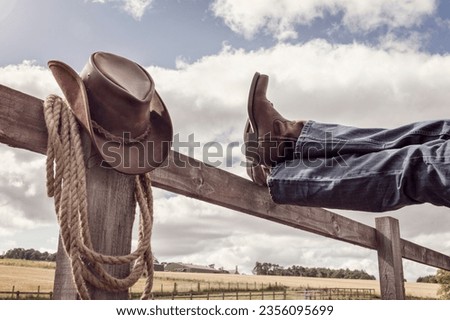 Cowboy boots and hat with feet up on stables fence at ranch resting with legs crossed, country music festival live concert or line dancing concept
