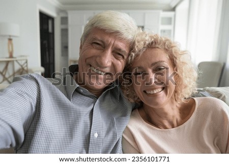 Happy carefree retired grey haired couple taking selfie at home, talking on video call, laughing, looking at camera, smiling at webcam, having fun. Screen view head shot portrait Royalty-Free Stock Photo #2356101771