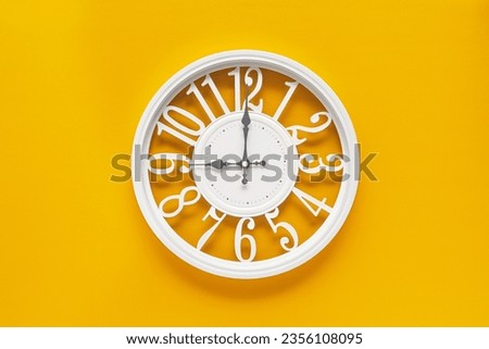 Modern white clock with a circle on a yellow wall background, nine o'clock on the clock. Elegant clock, combination of white and yellow colors