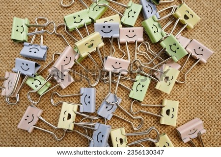 Pastel colored Office Paper Clips, Smiley Binder Clips, and Pencils on Notepad. Office supplies on aesthetic burlap background. Open spiral notebook on table. Knowledge or education. Back to school