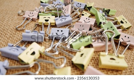 Pastel colored Office Paper Clips, Smiley Binder Clips, and Pencils on Notepad. Office supplies on aesthetic burlap background. Open spiral notebook on table. Knowledge or education. Back to school