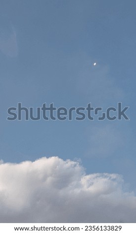 Photo of white clouds with a blue sky background.  There is a dot of the moon in the upper corner which is so detailed that it adds a beautiful impression