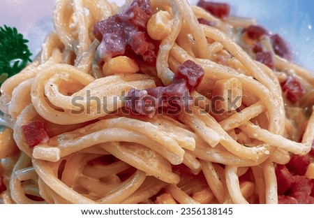 a photography of a plate of pasta with bacon and corn, carbonara with bacon and corn on a plate with parsley.