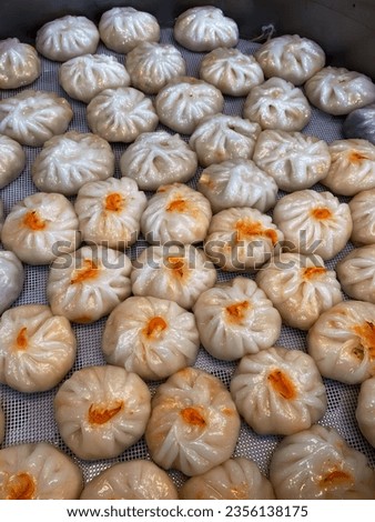 a photography of a bunch of dumplings sitting on a tray, doughnuts are lined up on a metal tray in a kitchen.
