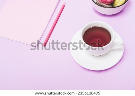 Pink notebook with a pencil and a cup of tea on a purple background, top view. Student breakfast