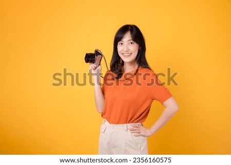 Young asian woman with camera isolated on yellow background, ready for a fun adventure tour. Positive holiday vibes concept.