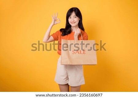 Celebrate savings and style in a shopping spree. Young woman holding bag isolated on yellow background, radiating happiness in a mall setting.