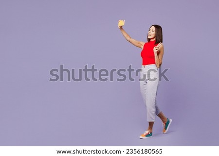 Full body young woman wears red tank shirt casual clothes doing selfie shot on mobile cell phone post photo on social network isolated on plain pastel light purple background studio. Lifestyle concept