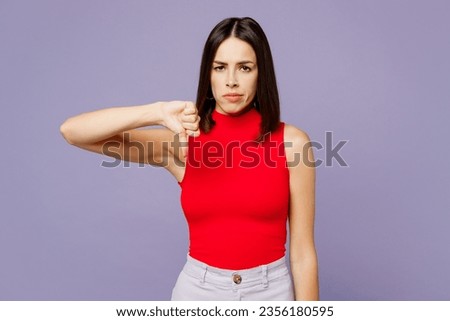 Young upset dissatisfied displeased woman wearing red tank shirt casual clothes showing thumb down dislike gesture isolated on plain pastel light purple background studio portrait. Lifestyle concept Royalty-Free Stock Photo #2356180595