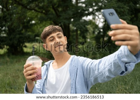 Smiling male traveler holds a plastic glass of bubble tea and take selfie on the street while vacation in Taiwan. Copy space