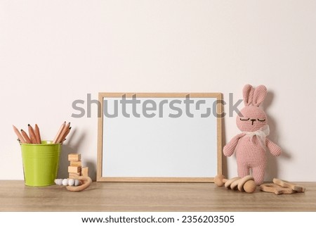 Empty square frame, stationery and different toys on wooden table