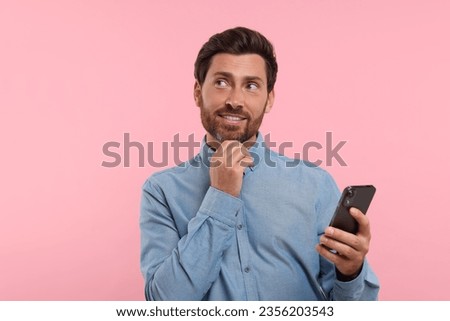 Handsome bearded man using smartphone on pink background