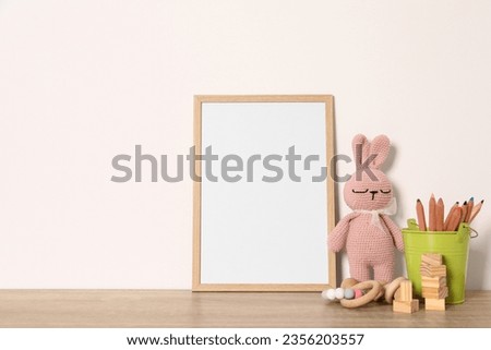 Empty square frame, stationery and different toys on wooden table, space for text