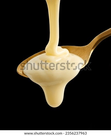 pouring condensed milk in golden spoon isolated on black background Royalty-Free Stock Photo #2356237963
