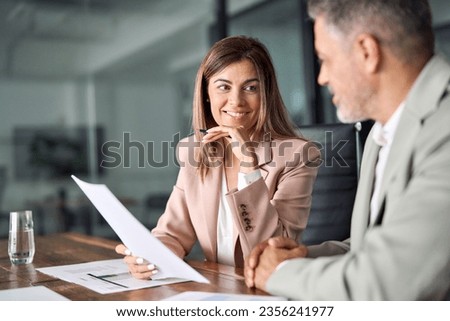 Two business executives discussing financial legal papers in office at meeting. Smiling female lawyer adviser consulting mid aged client at meeting. Mature colleagues doing project paperwork overview. Royalty-Free Stock Photo #2356241977