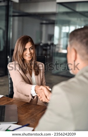 Happy mature Latin business woman manager lawyer handshaking client at office meeting. Smiling professional businesswoman and businessman shake having partnership agreement with handshake. Vertical Royalty-Free Stock Photo #2356242039