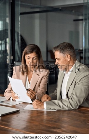 Mature business woman manager holding legal documents consulting client at office meeting, two professional executives experts discussing financial accounting papers working together. Vertical. Royalty-Free Stock Photo #2356242049