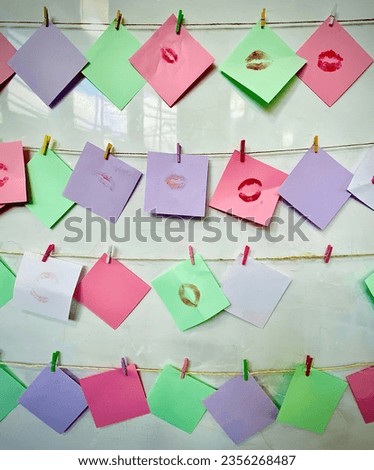 Lipstick mark on the pieces of colourful paper hanging with small clip on the big white board 