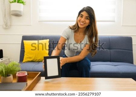 Happy beautiful woman smiling while putting a blank mock-up picture frame in her living room home