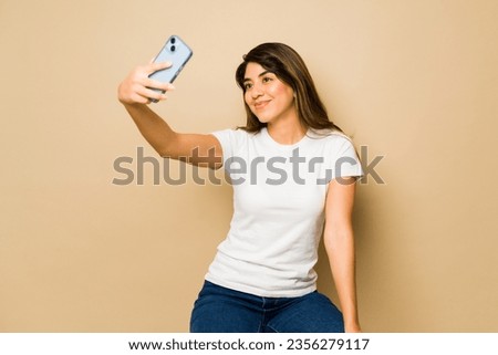Attractive mexican woman wearing a white mock-up t-shirt for a design taking a selfie in a studio background