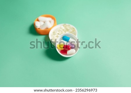 Pills capsules in a white bottle cap on green background. Drug, vitamin, tablets.  Royalty-Free Stock Photo #2356296973
