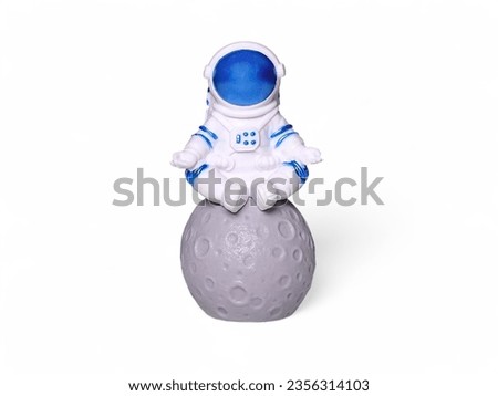 Miniature astronaut toy sitting on the moon on a white background