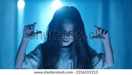 Little caucasian girl in ghost white sundress costume for halloween roaring into camera, frightening someone in hallway of haunted house 