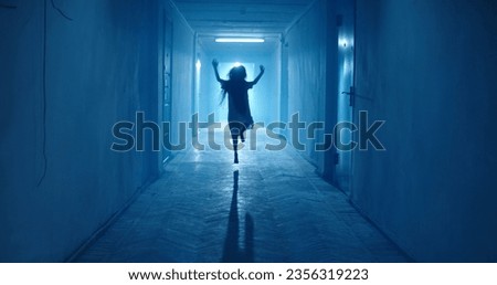 Little girl in white dress looking like a ghost carelessly running down the hallway of a haunted house - halloween costume party, horror movie 
