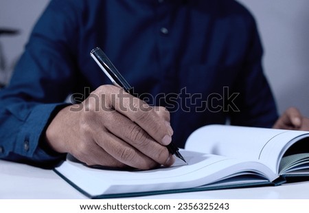 Close-up of a businessman using a pen and writing on paper, taking notes, making a business plan.