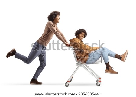 Caucasian guy pushing an african american young man inside a shopping cart isolated on white background