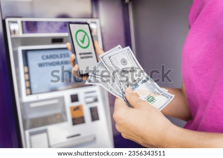Young woman using the smart phone for cardless withdrawing the cash near the ATM