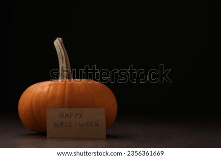 Small orange classic pumpkin on wood table with halloween paper card