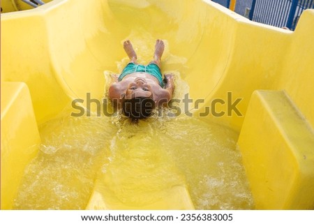  happy child slides down the yellow water slide in the water park. a joyful 10 year old boy has fun in the water park, riding down the hill.