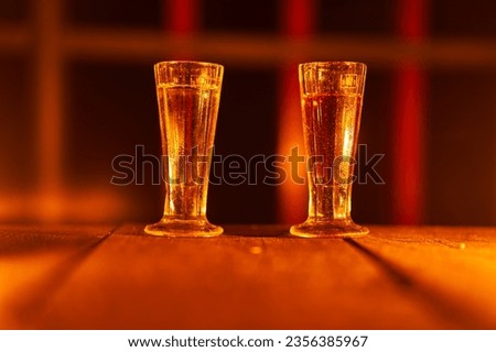 Two old vintage shot glasses with slivovitz on the old wooden table illuminated by orange candle lights. Picture is taken in the dark during hot summer midninght outdoor on the terrace of old house.