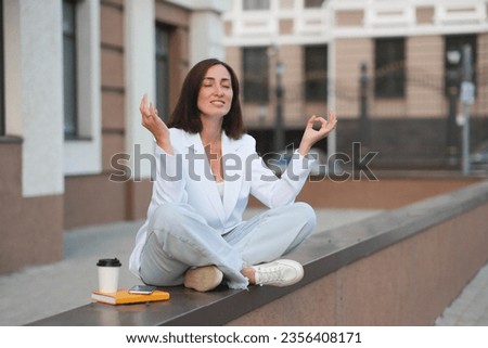 A young beautiful fashionable woman sits near a modern building and has relaxion and meditation after work day. Horizontal view.