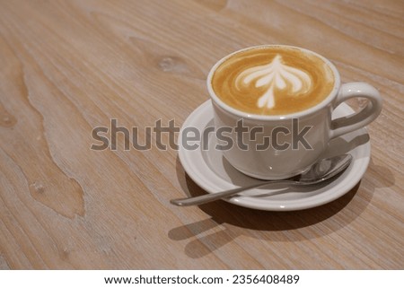 Flower cappuccino coffee art served with white cup and white spoon on wooden patterned table taken with good angle and lighting