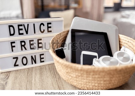 digital detox and technology concept - close up of device free zone words on light box and different gadgets in wicker basket on table at home