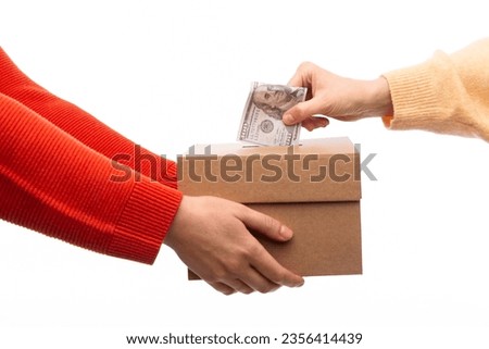 charity, savings and fundraising concept - close up of hand putting dollar cash money into donation box Royalty-Free Stock Photo #2356414439