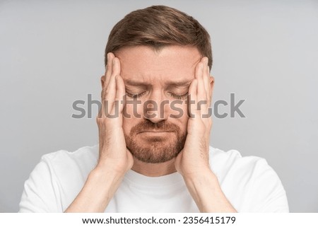 Portrait tired exhausted man feeling headache holding face hands with closed eyes on grey background. Bearded guy suffers head pain, migraine, cephalalgia, hypertension, disorder, sinus, cluster ache. Royalty-Free Stock Photo #2356415179