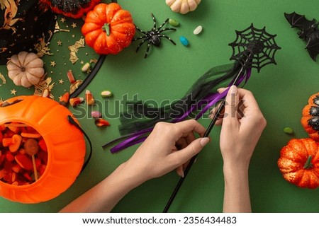 Dive into festive Halloween night celebration with this engaging representation. Observe a top-view picture capturing hand with magic wand and Halloween decorations on a green isolated backdrop